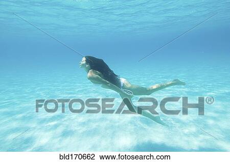 Stock Image - Underwater view of woman swimming in ocean. Fotosearch