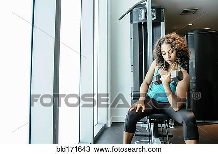 Stock Image - Woman lifting weights in gymnasium. Fotosearch