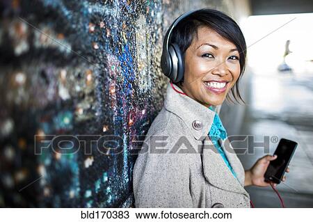 Stock Image - Woman listening to cell phone by mural. Fotosearch