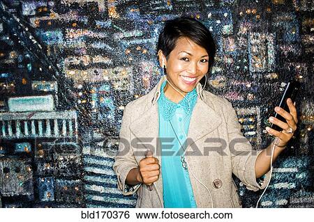 Stock Photograph - Woman listening to cell phone by mural. Fotosearch