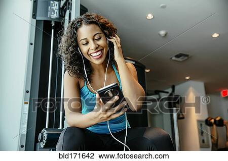 Woman listening to earbuds in gymnasium View Large Photo Image Stock Image - Woman listening to earbuds in gymnasium. Fotosearch