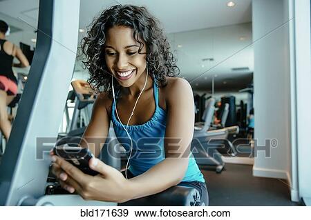 Woman listening to earbuds in gymnasium View Large Photo Image Stock Photo - Woman listening to earbuds in gymnasium. Fotosearch