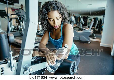 Picture - Woman resting on exercise machine in gymnasium. Fotosearch