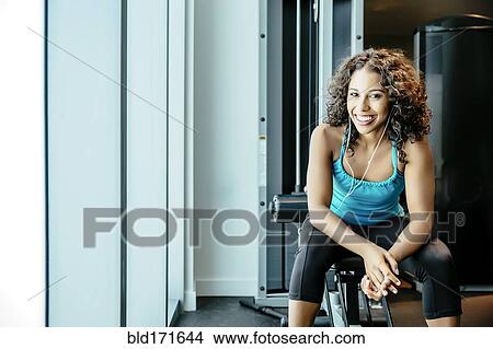Picture - Woman sitting on exercise machine in gymnasium. Fotosearch