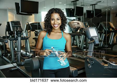 Stock Photo - Woman smiling near exercise machines in gymnasium. Fotosearch