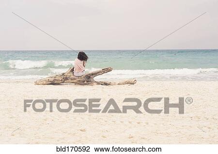 Stock Image - Woman sunbathing on driftwood log on beach. Fotosearch