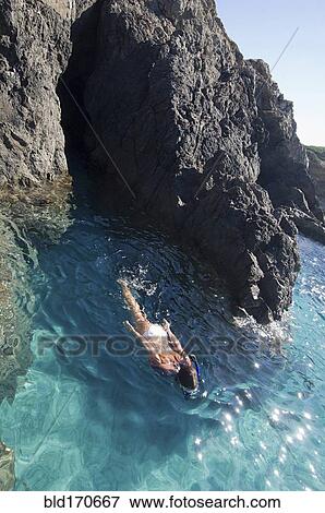 Woman swimming in ocean by rocky cliffs View Large Photo Image Stock Photo - Woman swimming in ocean by rocky cliffs. Fotosearch