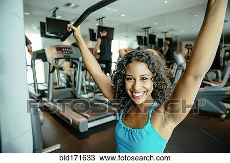 Stock Image - Woman using exercise machine in gymnasium. Fotosearch
