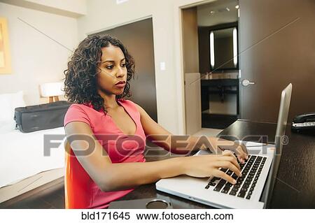 Stock Photography - Woman using laptop at desk in hotel room. Fotosearch