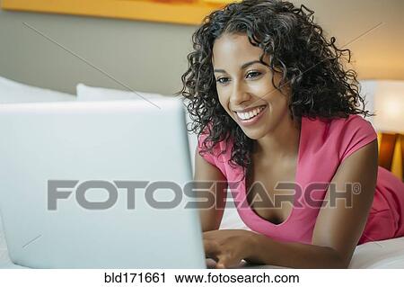 Stock Image - Woman using laptop on hotel bed. Fotosearch