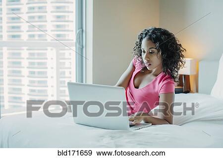 Stock Photo - Woman using laptop on hotel bed. Fotosearch