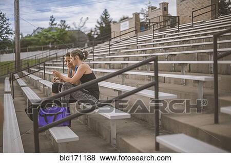 Stock Photo - Women using cell phone on bleachers. Fotosearch