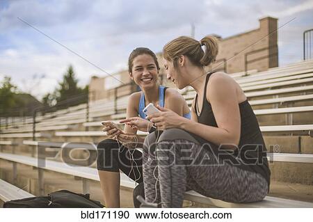 Stock Image - Women using cell phones on bleachers. Fotosearch