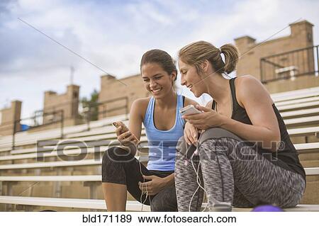 Stock Photo - Women using cell phones on bleachers. Fotosearch