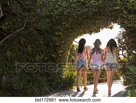 Stock Image - Women walking under shrub arch in garden. Fotosearch