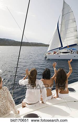 Stock Image - Women waving from sailboat on ocean. Fotosearch
