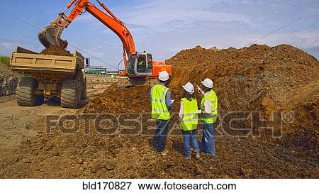 Stock Photo - Workers watching digger machinery in field. Fotosearch