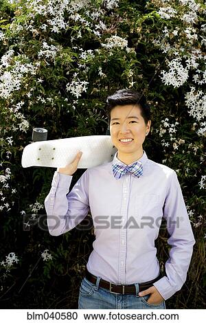 Stock Image - Androgynous woman holding skateboard. Fotosearch