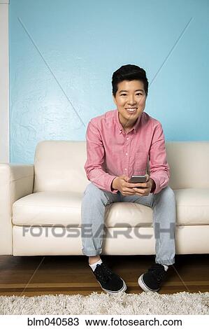 Stock Image - Androgynous woman using cell phone on sofa. Fotosearch