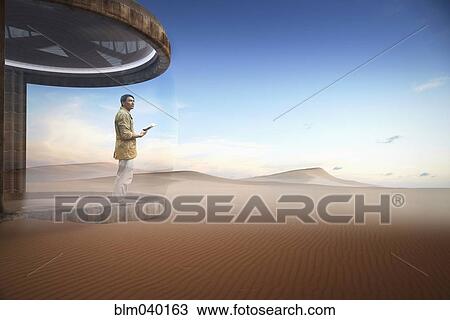Stock Image - Asian man standing on patio in desert. Fotosearch