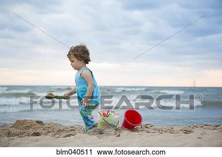 Stock Image - Caucasian baby girl playing on beach. Fotosearch