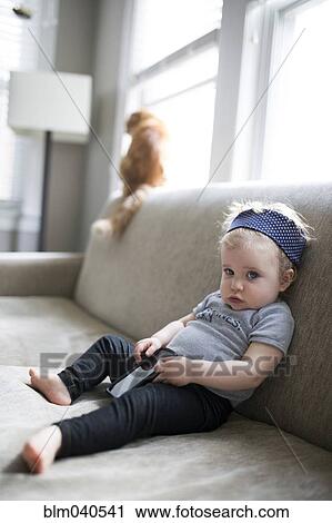 Stock Image - Caucasian baby girl sitting on sofa. Fotosearch