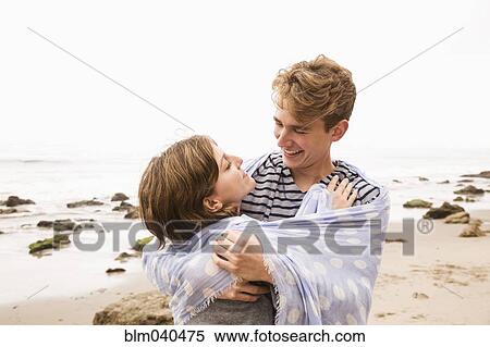 Stock Photography - Caucasian couple wrapped in blanket on beach. Fotosearch