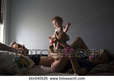 Stock Photograph - Caucasian father and children playing on bed. Fotosearch