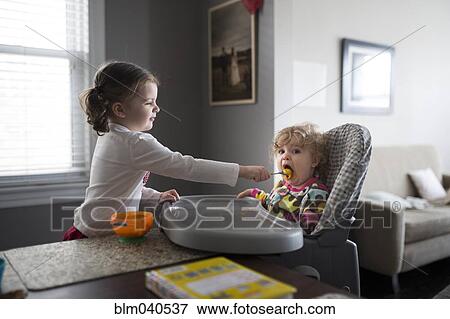 Stock Photo - Caucasian girl feeding baby sister. Fotosearch