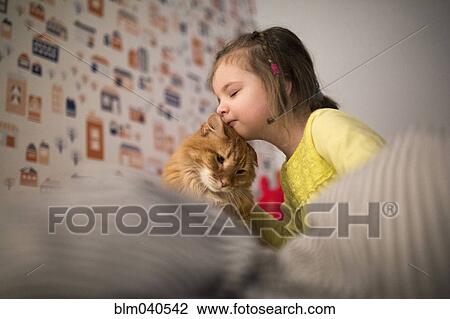 Stock Image - Caucasian girl hugging cat on bed. Fotosearch