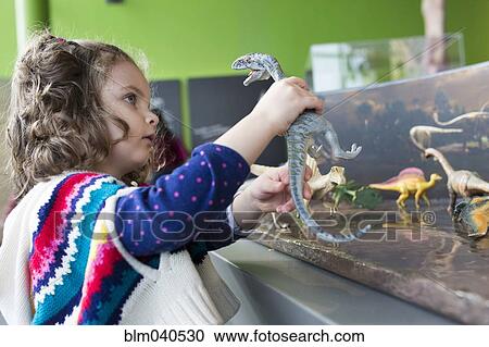 Stock Image - Caucasian girl playing with dinosaur toys. Fotosearch