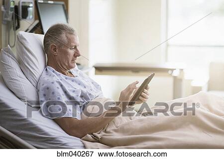 Stock Photo - Caucasian patient using digital tablet in hotel bed. Fotosearch