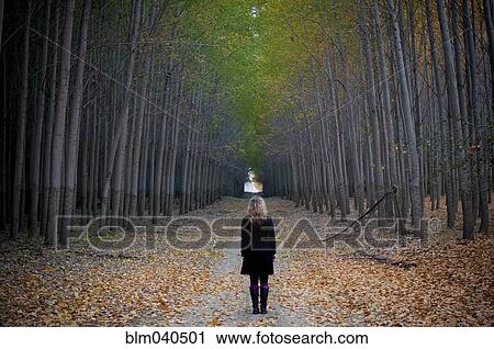 Stock Image - Caucasian woman standing on path between trees. Fotosearch