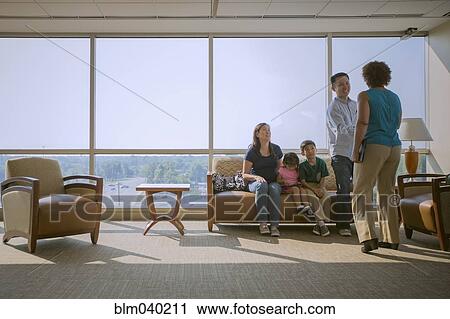 Stock Image - Doctor greeting patients in waiting room. Fotosearch