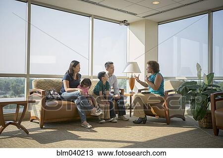 Stock Image - Doctor talking to patients in waiting room. Fotosearch