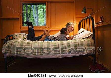 Stock Image - Father and daughter reading on bed. Fotosearch