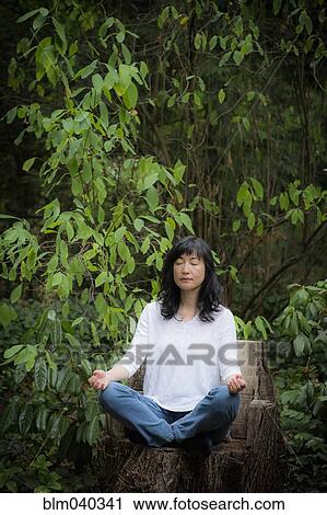 Stock Image - Japanese woman meditating in garden. Fotosearch