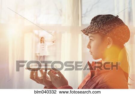 Stock Image - Mixed race girl examining hologram projection. Fotosearch