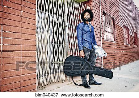 Stock Photo - Mixed race man carrying guitar outdoors. Fotosearch