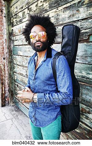 Stock Image - Mixed race musician carrying guitar outdoors. Fotosearch