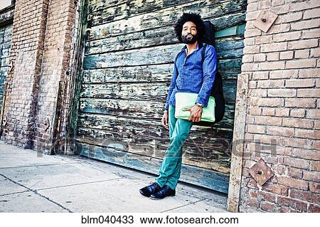 Stock Image - Mixed race musician carrying laptop outdoors. Fotosearch