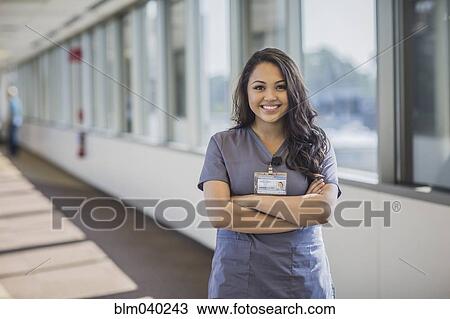 Stock Image - Mixed race nurse smiling in hospital hallway. Fotosearch