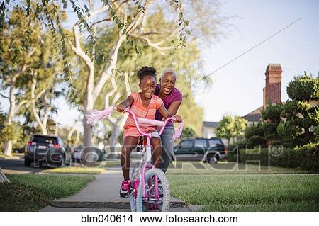 Picture - Mother pushing daughter on bicycle. Fotosearch