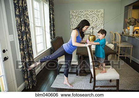 Stock Photograph - Mother stretching with son in dining room. Fotosearch
