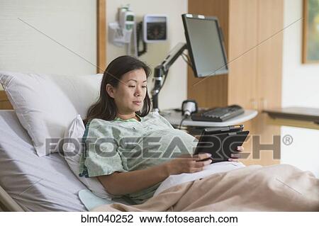 Stock Image - Pregnant Chinese woman in hospital room using digital tablet. Fotosearch
