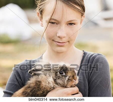 Picture - Serious girl holding rabbit on farm. Fotosearch