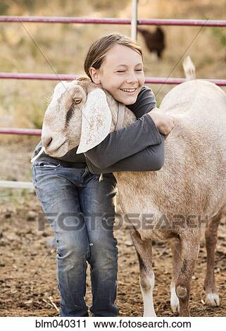 Stock Image - Smiling girl hugging goat on farm. Fotosearch