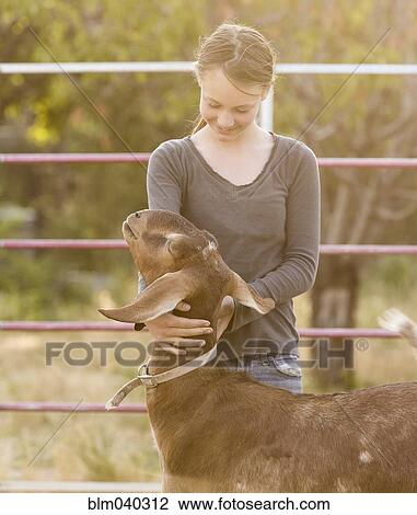 Stock Image - Smiling girl hugging goat on farm. Fotosearch