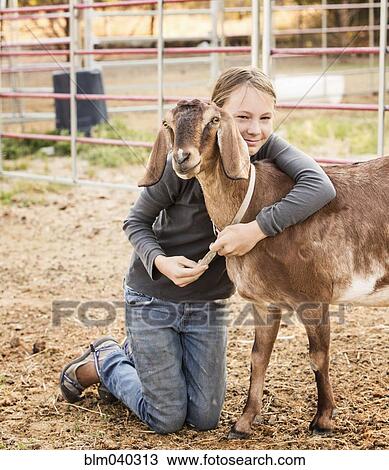 Stock Image - Smiling girl hugging goat on farm. Fotosearch