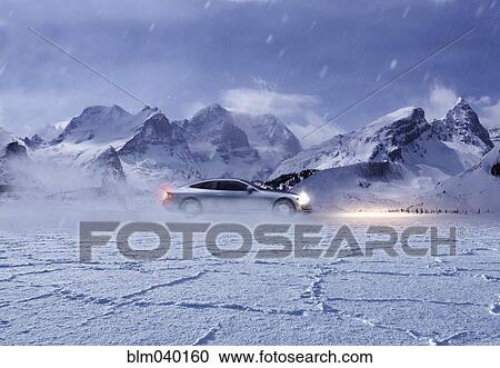 Stock Image - Sports car driving in snowy remote landscape. Fotosearch